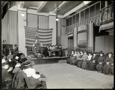 Mensen in een auditorium bij de New York Association for the Blind met kerstboom en mensen die mogelijk een sketch opvoeren op het podium met orgel, 1920 door Byron Company